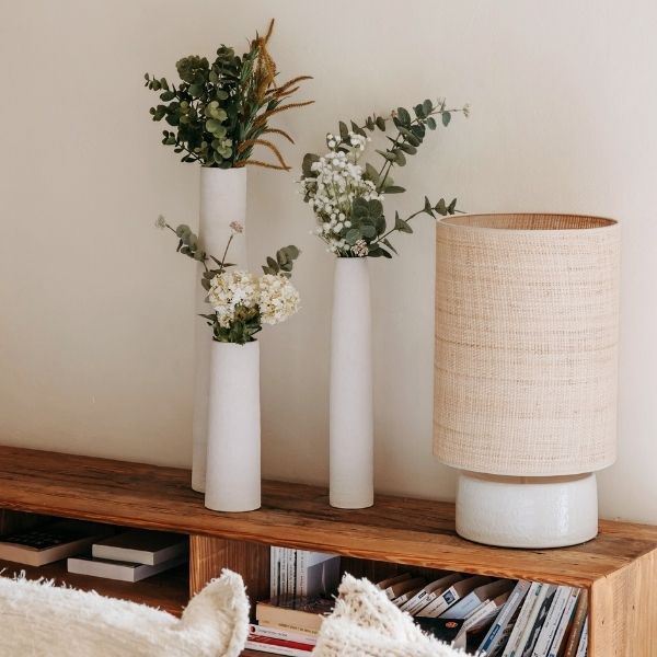 Luminaire en raphia et vases blancs sur un meuble en bois